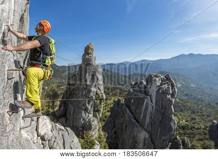 Male climber in special outfit climbing cliff with mountaineering equipment