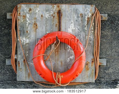 life buoy on a weathered wooden board with faded orange rope harbour