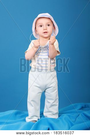 Serious kid stands against a blue background wearing a sailor suit