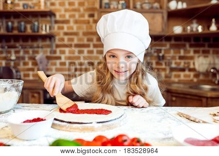 Little Girl Putting Tomato Sauce On Pizza Dough