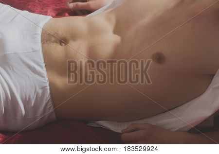 Seduction flirting and foreplay. Female hand touching sexy naked fit muscular male torso with six pack six packs abs ab in white briefs underwear on red bed