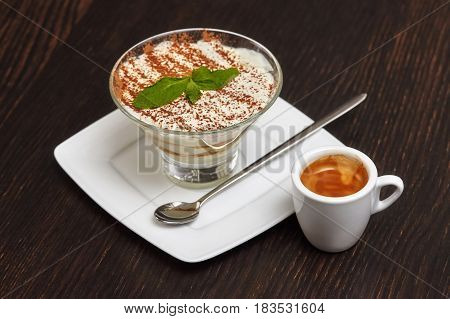 Tiramisu creme cake dessert in glass with mint leaves and coffee cup on black wooden background