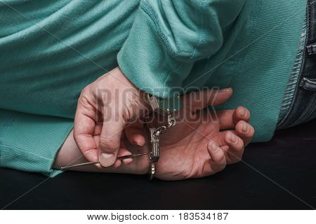 Lying hostage on the floor with hands behind trying to open handcuffs with a piece of wire.