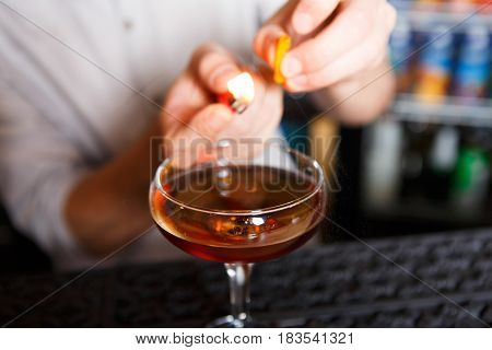 Barman's hands in bar interior making alcohol flaming cocktail. Professional bartender at work in bar mixing drink with burning fire. Party time in night club