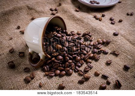 White Cup full of roasted coffee beans on rustic old cloth.