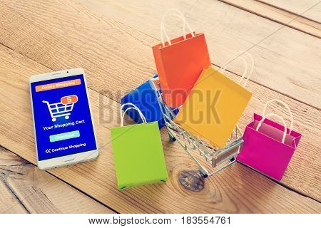 White smartphone runs an online shopping app put near colorful paper shopping bags and a shopping cart. Consumers can buy everything from online stores using a smart device connects to the internet.