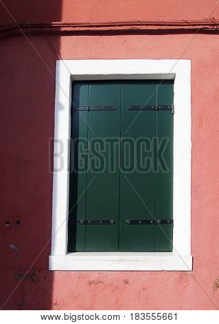 Green shuttered window in a white frame on a pink wall