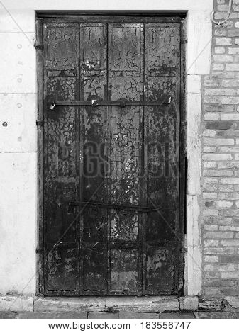 Old wooden door with peeling paint and rusting hinges in an ancient brick wall