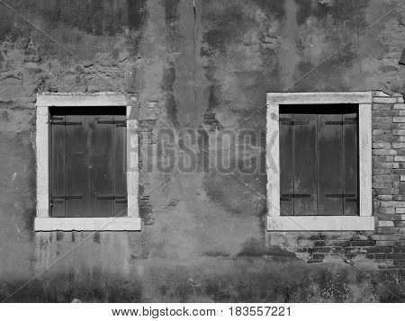 old distressed painted wall with two wooden shuttered windows and white window frames