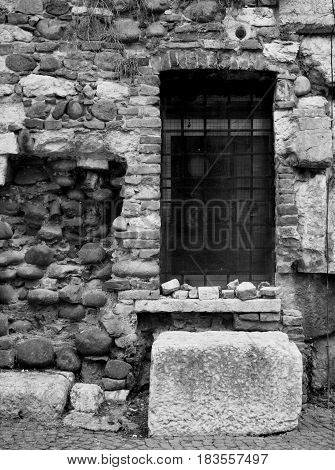 old damaged and repaired brick wall with a barred window and old stones in monochrome