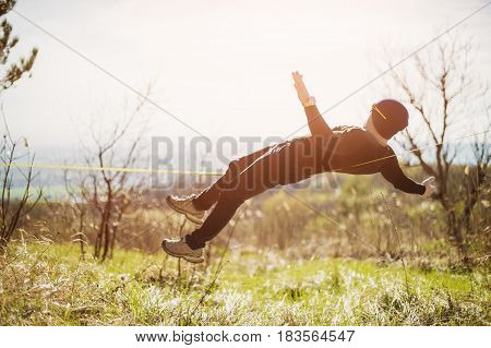 A man with a beard and in sunglasses lying balancing a stretching rope or an open-air canopy under the open sky, a slaskening nature in the spring, a balance, a learning concept