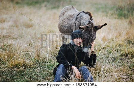 The young guy sits near the donkey. Friendship between man and animals in greenpeace.