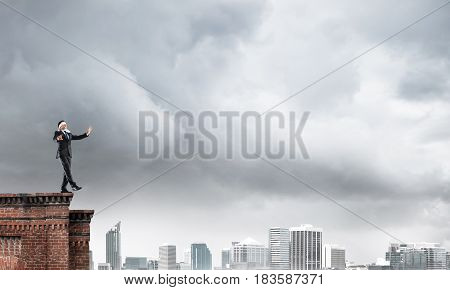 Businessman with blindfold on eyes walking on building top