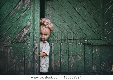 A terrible old doll at the old gate. Vintage background. Concept for poster and billboard.