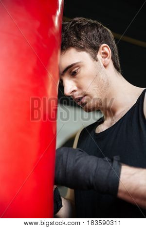 Tired man boxer wearing gloves leaning on red punchbag