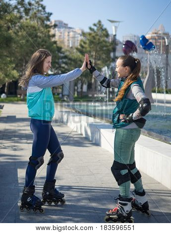 Two roller girls giving hive five in the park. Meeting of friends for roller skating. They are smiling