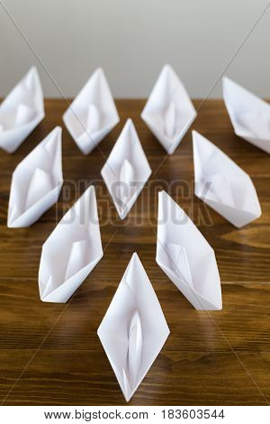 Origami white paper boats on a wooden table, soft focus.