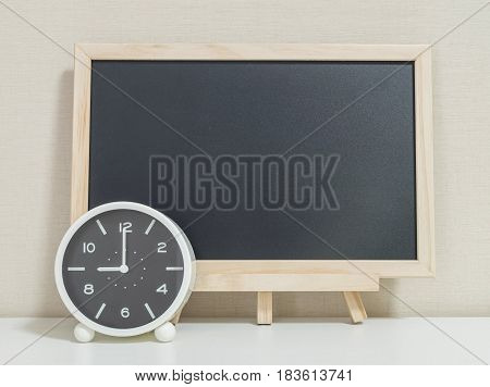Closeup alarm clock for decorate show 9 o'clock with wood black board on white wood desk and cream wallpaper textured background selective focus at the clock
