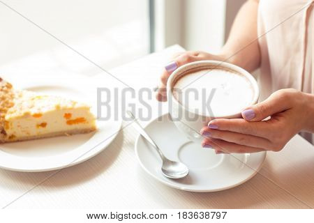 A beautiful young woman sitting in a cafe. Girl drinks Cappuccino.