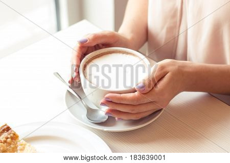 A beautiful young woman sitting in a cafe. Girl drinks Cappuccino.
