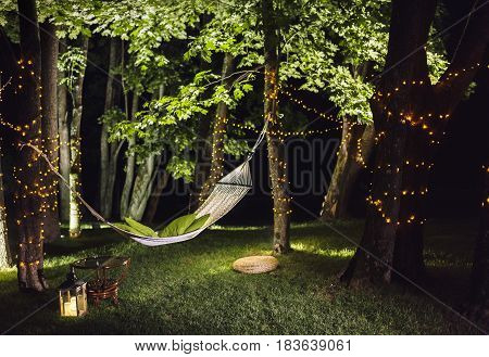 Hammock weighs in the forest at night. forest illuminated garlands of light bulbs. Trees illuminated lanterns