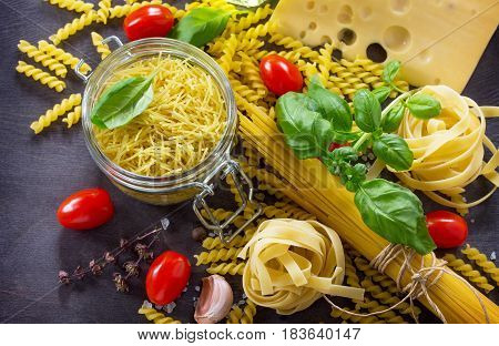 Various Kinds Of Pasta Ingredients With Basil, Cherry Tomato, Garlic, Pepper And Cheese On Wooden Ki