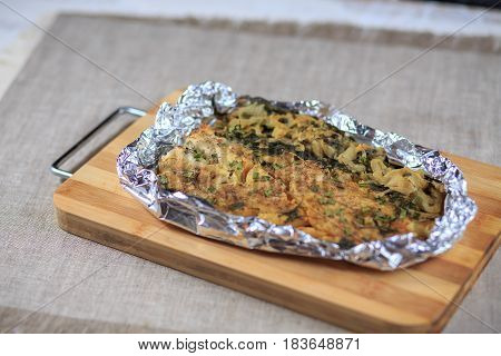 Fillet Of The Baked Fish In Seasonings And Greens In A Foil On A Board