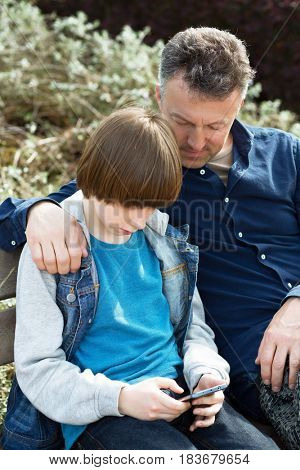 Father with teen son using smart phone outdoor together. Young boy with his father in spring park.