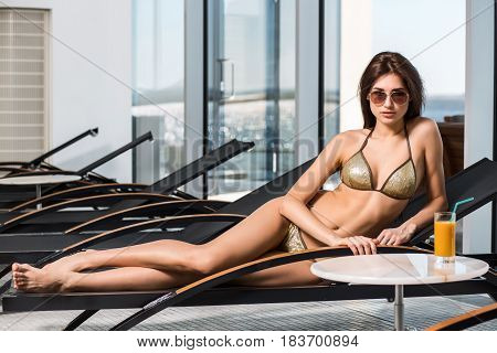 Body care. Woman with perfect body in bikini lying on the deckchair by swimming pool at resort spa hotel.