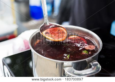 Making mulled wine for sale at country fair. Glintwine with spices, citrus and cloves in big metal stock pot, mixed with soup ladle.