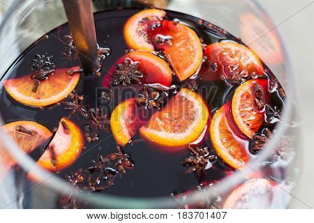 Making hot alcohol, mulled wine for sale at country fair. Glintwine from red wine with citrus and cloves in big glass, mixed with soup ladle. Closeup