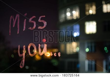 Miss you inscription (text) by lipstick on the window glass in the night. Love and miss concept. Valentine blurred background.