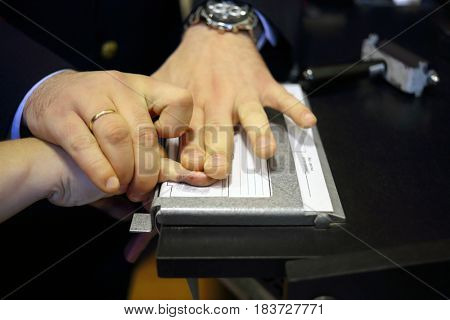 Hands of two men during fingerprinting, text translate - dactyloscopic registration, pinky