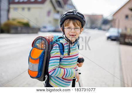 Active school kid boy in safety helmet riding with his scooter in the city with backpack on sunny day. Happy child in colorful clothes biking on way to school. Safe way for kids outdoors to school.