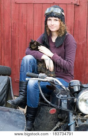 Photo of girl on vintage motorbike in pilot cap with cat