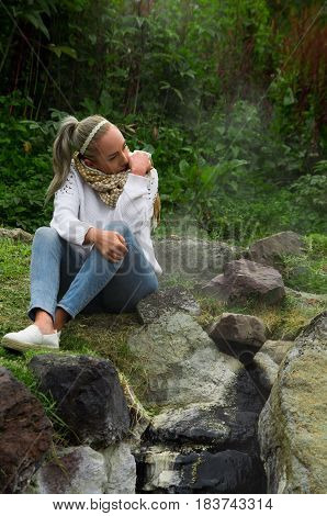 Pretty young pensive girl sitting by some rocks in a forest