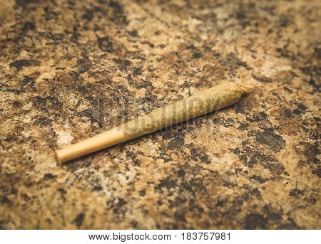 Pre-rolled joint or cigarette sitting on a textured counter top.