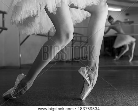 Ballerina in pointe shoes and a pack stands on the fingers of the machine. Reflection in the mirror in the ballet class. Classical ballet. Prima ballerina. Shooting close-up. Black and white photography