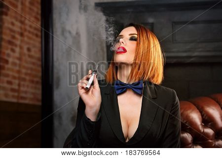 Young attractive girl in a jacket and bow tie smokes electronic cigarette. Femme fatale. Evening makeup smokey eye.