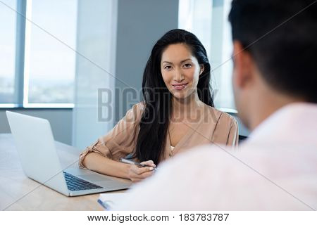 Young businesswoman sitting with male colleague at table in office