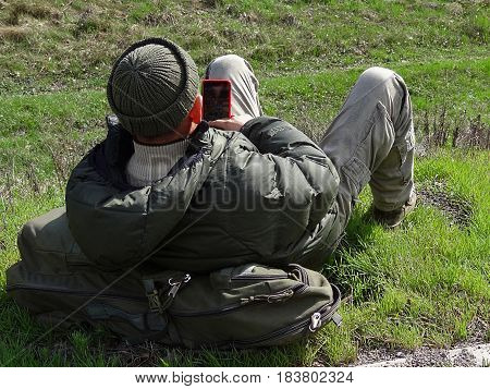 Soldier lies on grass and backpack holding phone in hand