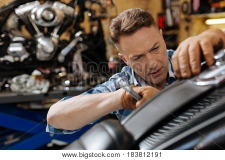 Better check it tice. Worried attentive skilled worker spotting an untied bolt on vintage bike and drawing it up using special wrench