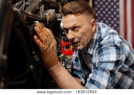 Final touches. Mature virile skilled expert looking carefully on bikes mechanisms while fixing it and polishing it to perfection