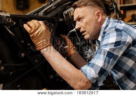 Closer look. Successful gifted accomplished serviceman using a wrench for untying a bolt and taking bikes heart out for maintenance