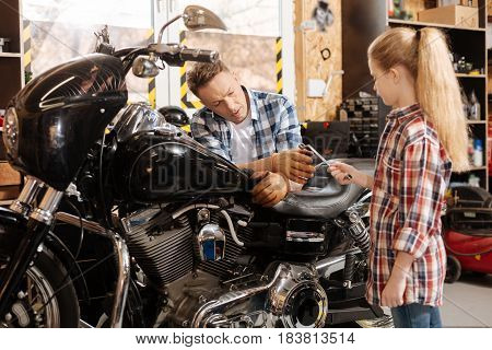 Little helper. Supportive intelligent cute child giving her father wrench he asking for while repairing his motorbike