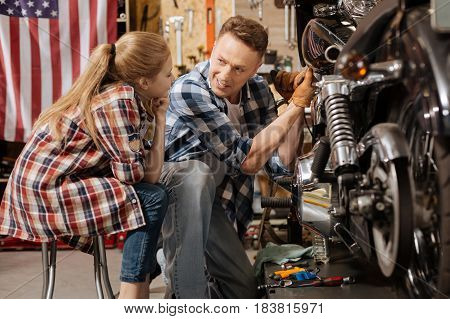 Attentive listener. Beautiful smart bright child being curious about what her dad doing while he repairing a bike