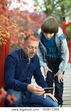 Father with teen son using smart phone outdoor together. Young boy with his father in spring park.