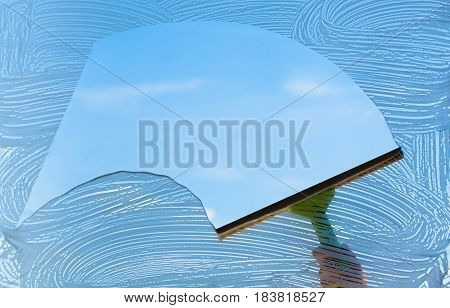 Human hand cleaning window from outside over sky background