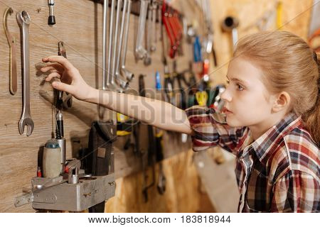 Is it heavy. Passionate energetic determined girl spending time at fathers garage and examining things while reaching for a wrench on the wall