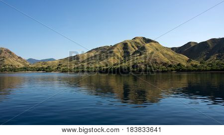 Coastline of mountains with green vegetation reflected in blue ocean water at Labuan Bajo in Flores Indonesia.